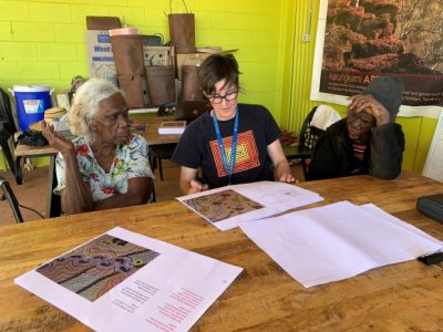 Three people sitting at a table looking at book.